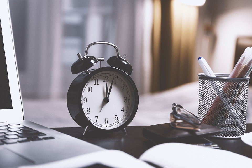 Clock on black desk next to laptop and reading glasses