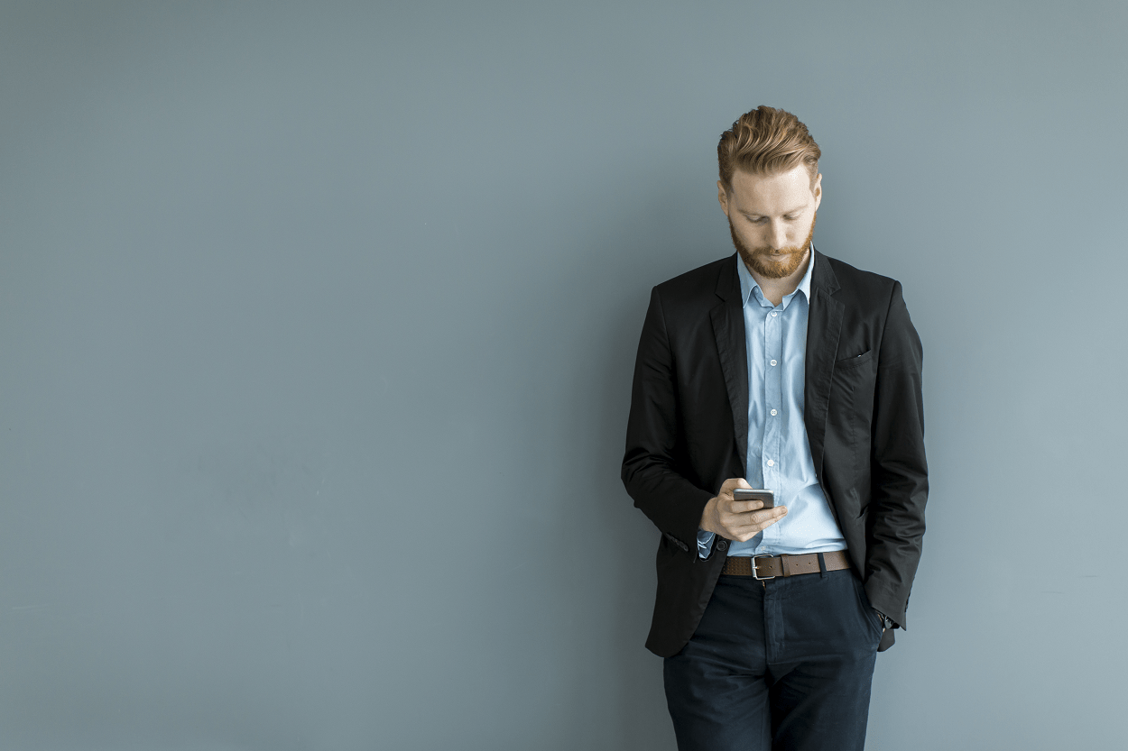 professional man using smartphone in front of grey wall
